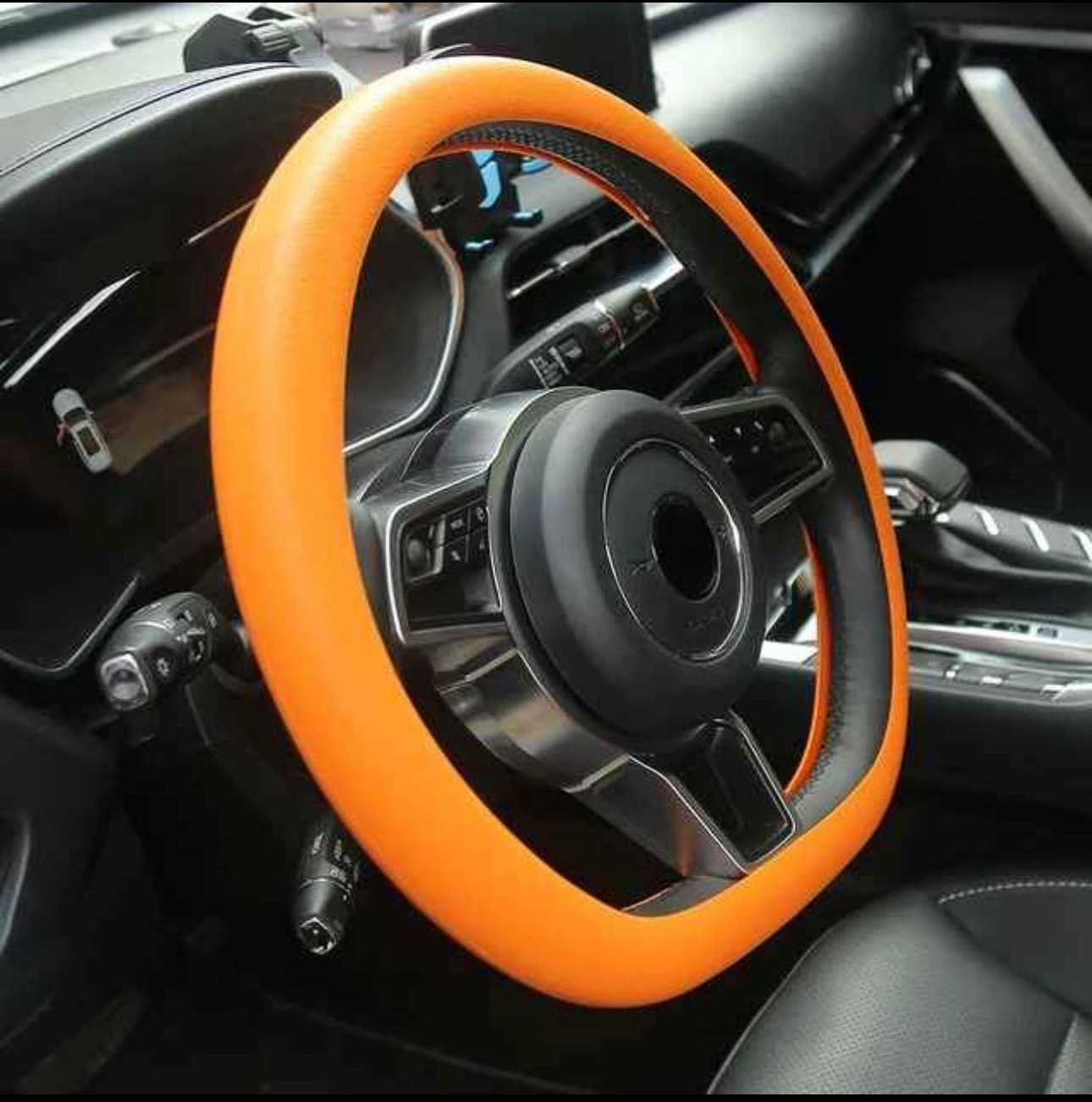 Volante de coche con forro de silicona naranja antideslizante, instalado en interior de vehículo, mejora agarre y protege del calor.