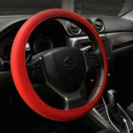 Volante de coche con forro de silicona roja antideslizante, instalado en interior de vehículo Suzuki, mejora agarre y protege contra calor.