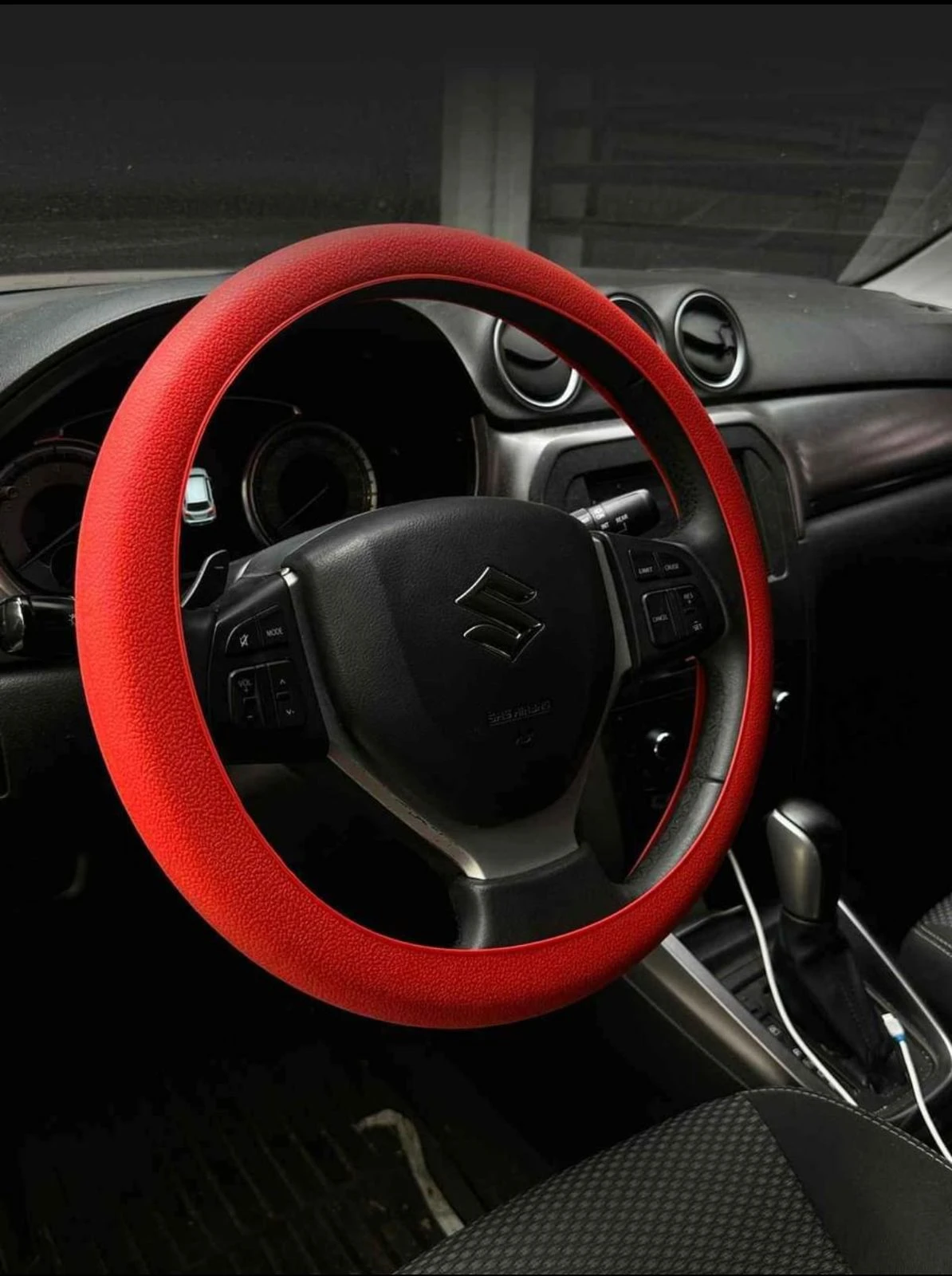 Volante de coche con forro de silicona roja antideslizante, instalado en interior de vehículo Suzuki, mejora agarre y protege contra calor.
