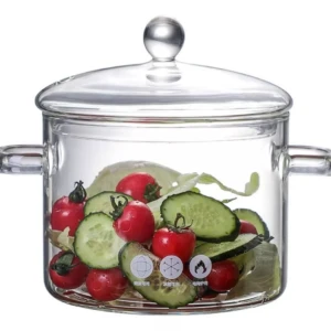 Olla de vidrio transparente con tapa y asas laterales, mostrando vegetales frescos como tomates cherry, pepino y lechuga.