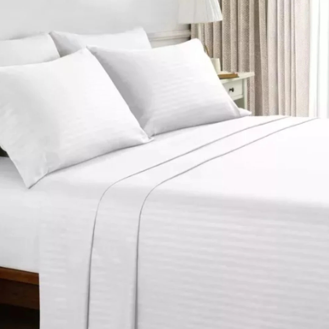 Sábana blanca de algodón y poliéster con textura suave, vista frontal en cama con cojines y sábanas a juego.
