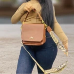 Carriel Dacota Dama Velez en cuero sintético marrón, con asa corta y correa larga estampada, usado por mujer con jeans y top beige.