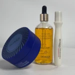 Kit de cuidado facial y capilar Bioaola con suero de colágeno en frasco de vidrio ámbar, mascarilla facial en tarro azul y tratamiento capilar en tubo blanco, dispuestos sobre superficie blanca.