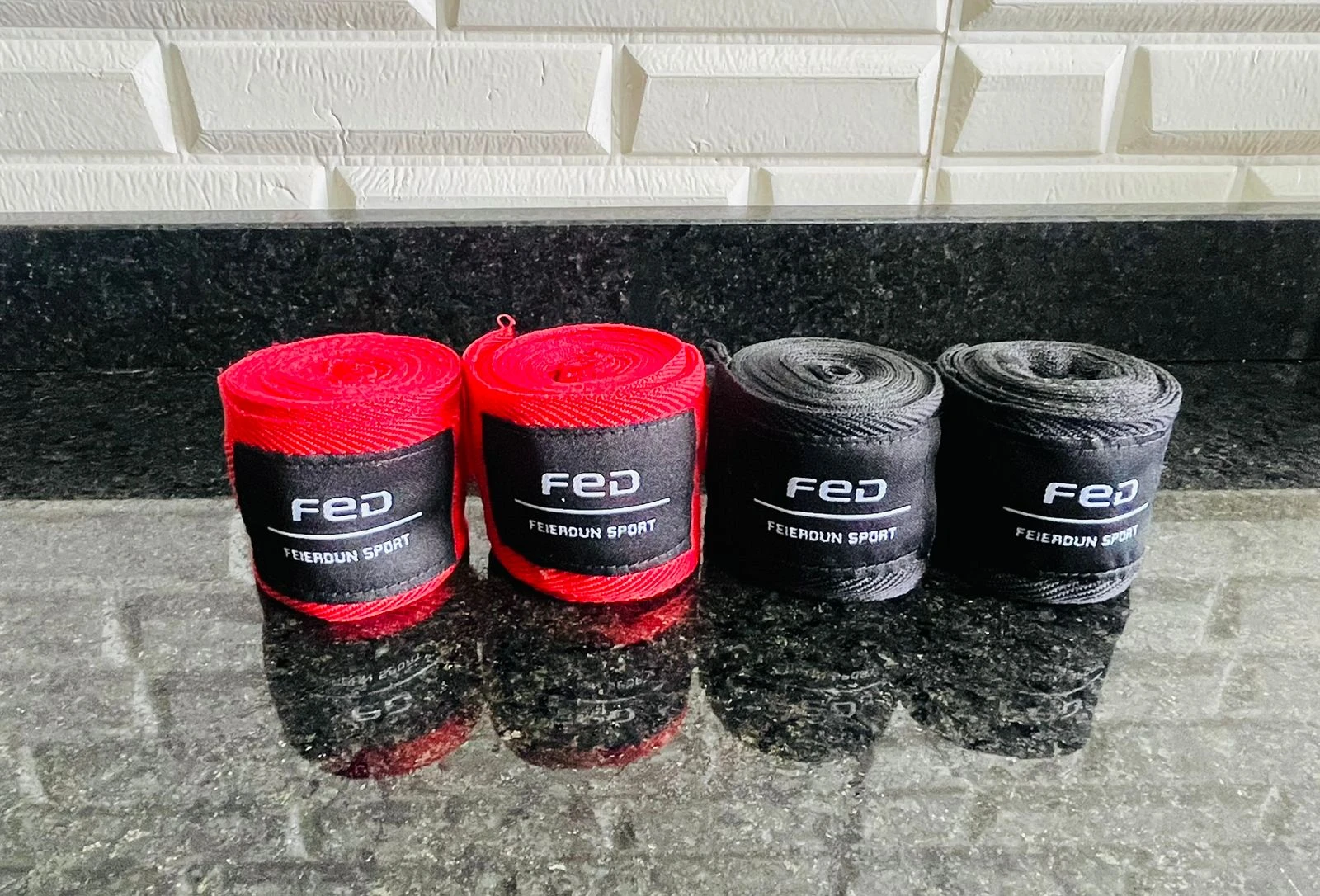 Cuatro vendas de boxeo enrolladas en rojo y negro, con la marca FED y el texto "FIERDOUN SPORT" visible, sobre una superficie oscura brillante.