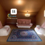 Alfombra persa de 2x1,50m con base antideslizante, diseño tradicional en tonos azules y rojos sobre fondo oscuro, colocada en sala de estar con sofá y sillones.