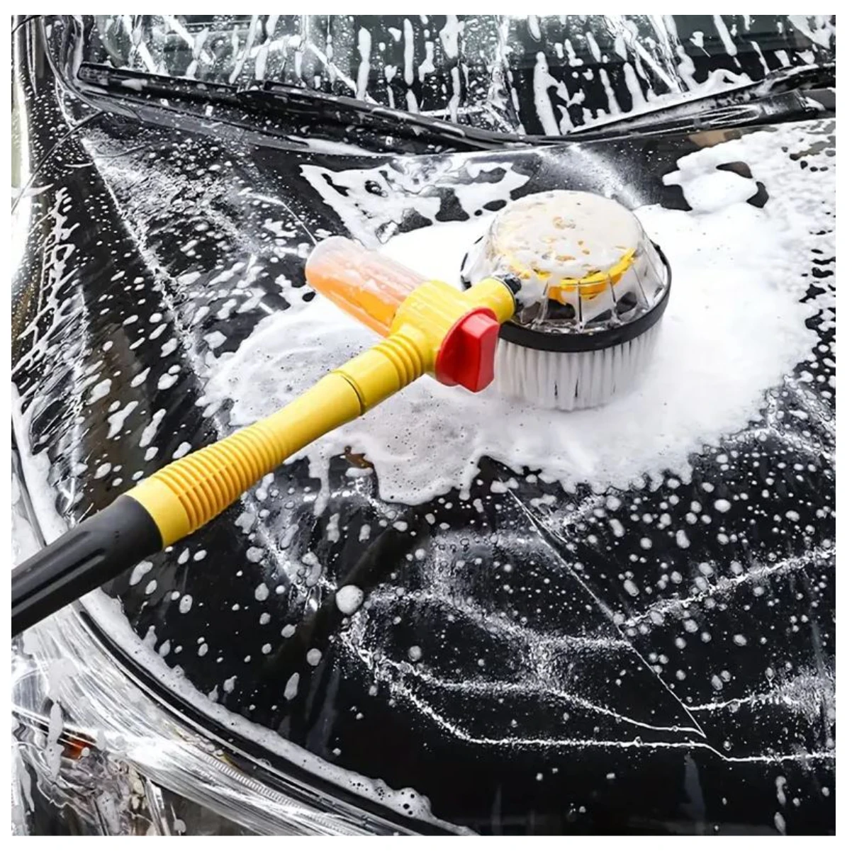 Cepillo de lavado automático para autos con cerdas chenille, mango amarillo y cabezal rotatorio en acción sobre carro negro con espuma.