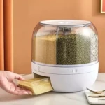 Dispensador giratorio blanco con tres compartimentos visibles de granos: mijo, lentejas y arroz, con dispensador frontal en uso sobre mesa.