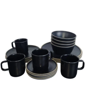 Vajilla de melamina color negro con tazas, platos y bowls apilados sobre fondo blanco.