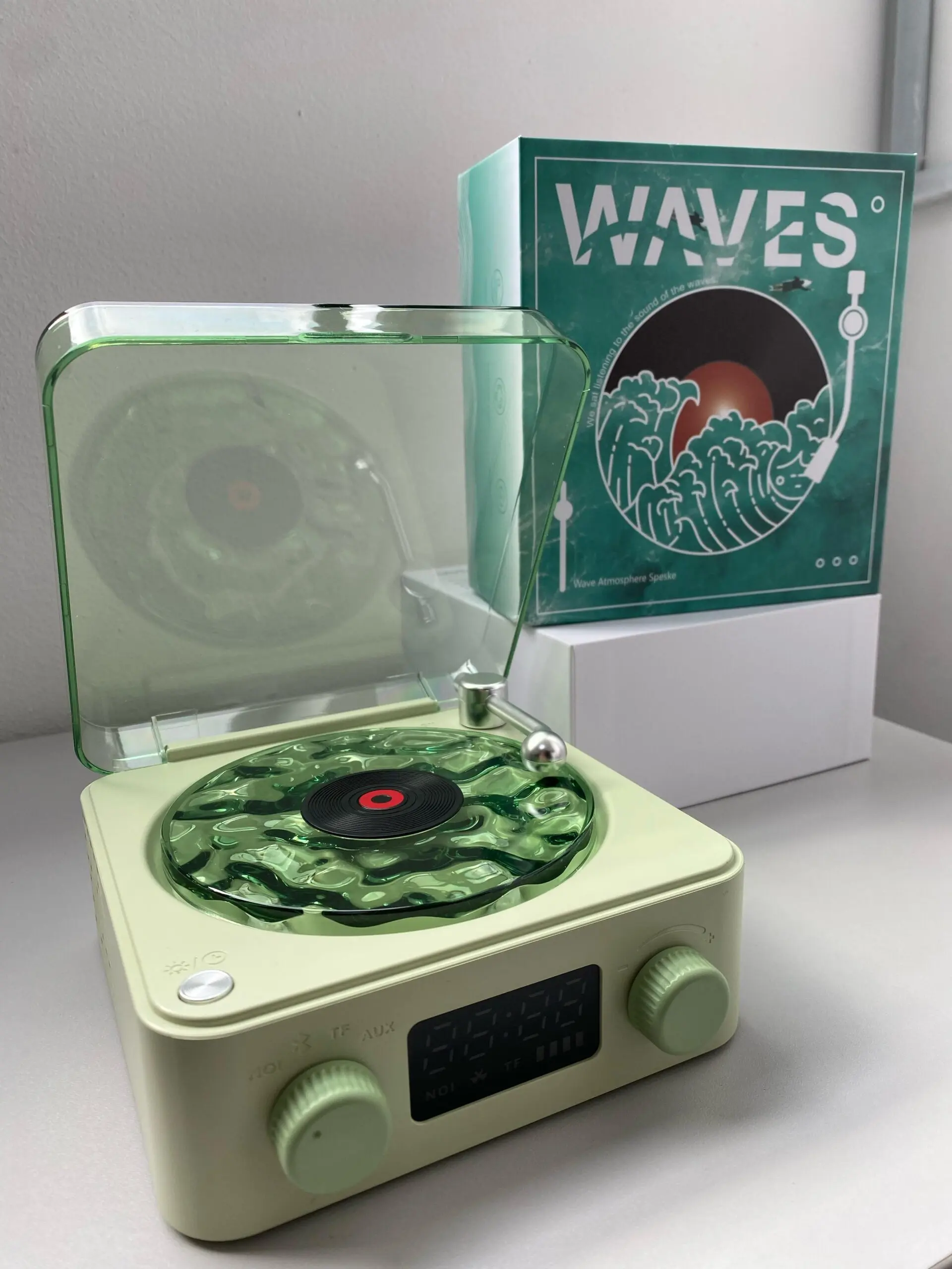 Tocadiscos retro en color verde menta con disco transparente y caja de presentación, mostrando detalles como botones giratorios y pantalla digital.