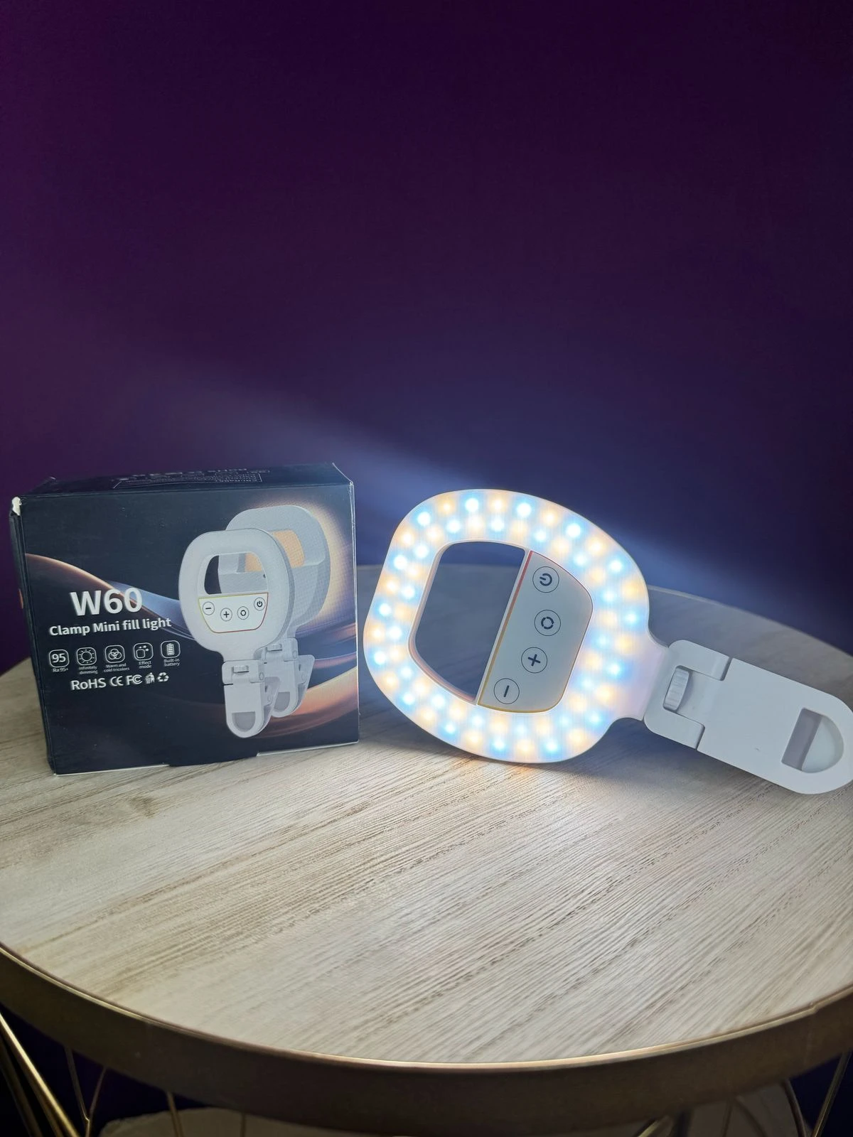 Aro de luz LED difusa con control táctil, encendido en tono cálido, sobre mesa de madera clara junto a su caja negra. Ideal para selfies y videollamadas.