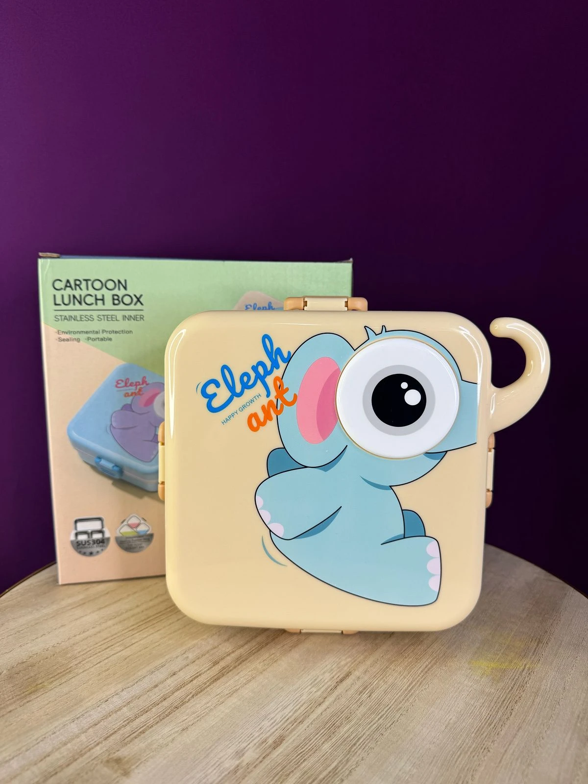 Lonchera térmica de acero inoxidable color crema con diseño de elefante azul, tapa con asa y caja de cartón al fondo.