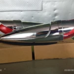 Dos tubos de escape estilo bala misil en acabado cromado brillante, con detalles rojos visibles en la parte trasera, colocados sobre cajas de cartón.