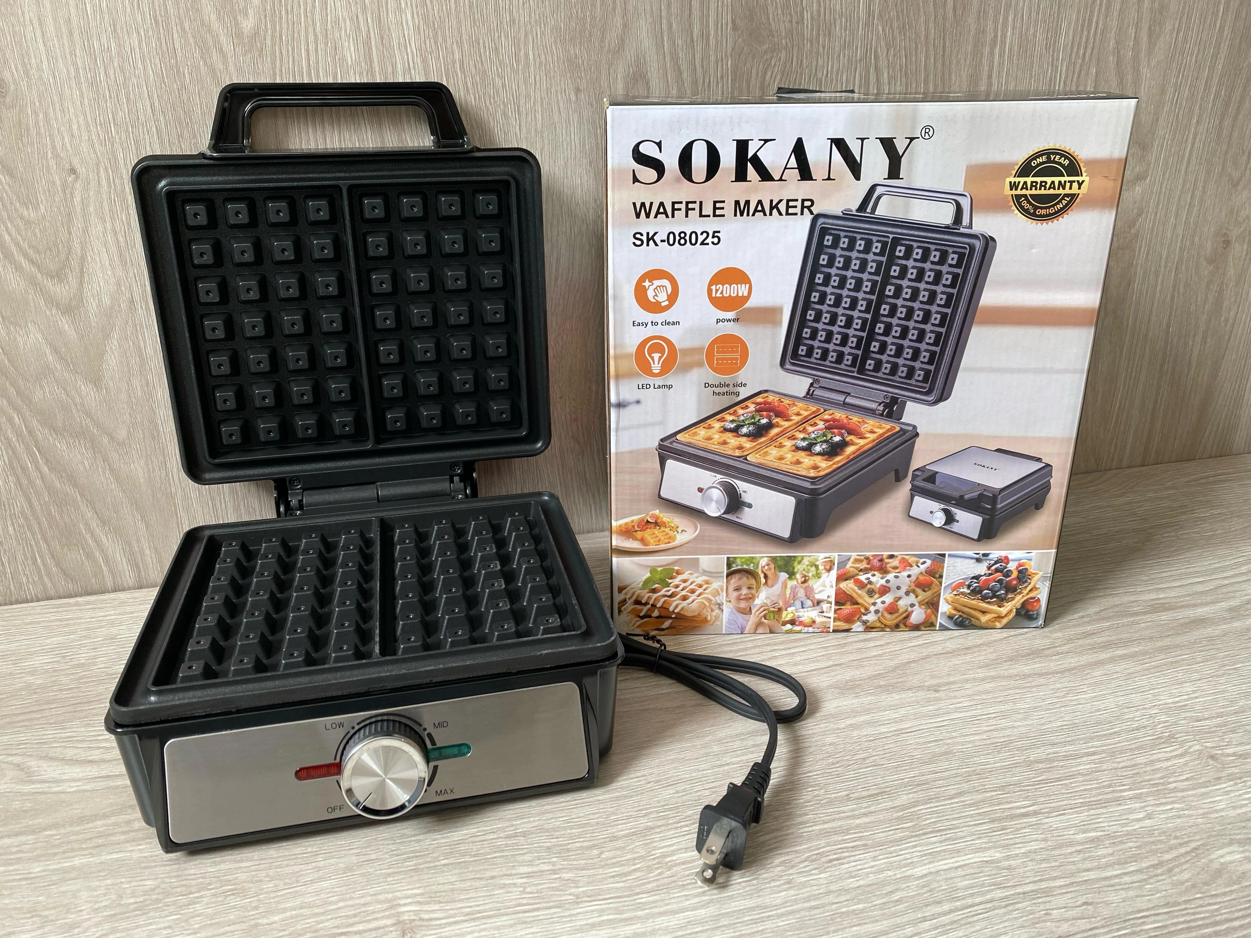 Waflera Sokany SK-08025 de color negro, con tapa abierta mostrando la rejilla interior y panel frontal con perilla de control, junto a su caja de cartón con ilustraciones de uso.