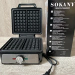 Waflera Sokany de 1200W, color negro, con tapa abierta mostrando placas de cocción y panel frontal con perilla de control, junto a su caja original.