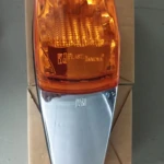 Indicador lateral compacto con carcasa cromada y lente ámbar, montado sobre caja de cartón.