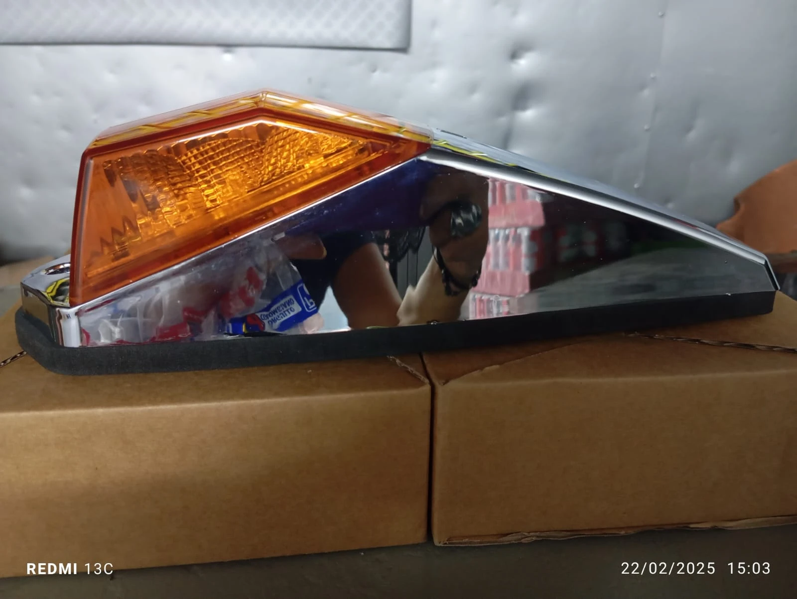 Indicador lateral compacto con carcasa cromada y lente ámbar, colocado sobre cajas de cartón.