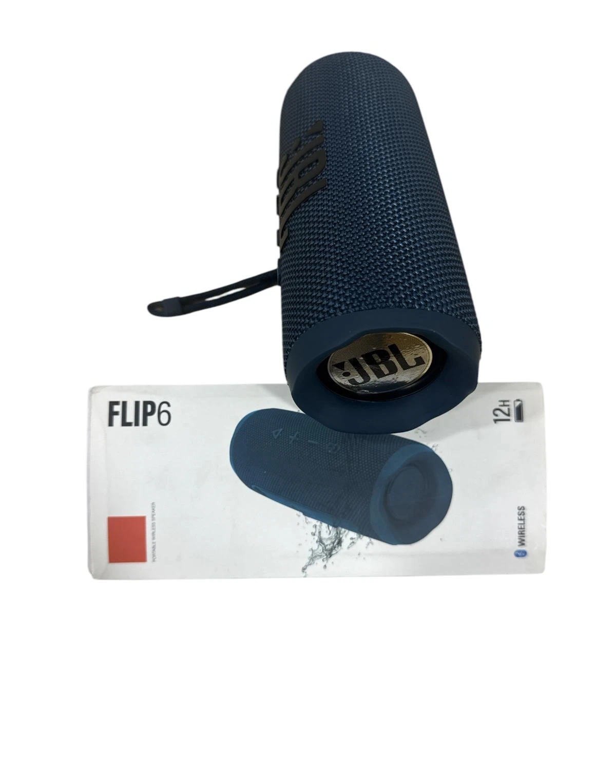 Altavoz JBL Flip 6 en color azul oscuro, con textura de malla y asa negra, colocado sobre su caja de cartón blanco que muestra el modelo y una representación del producto sumergido en agua.