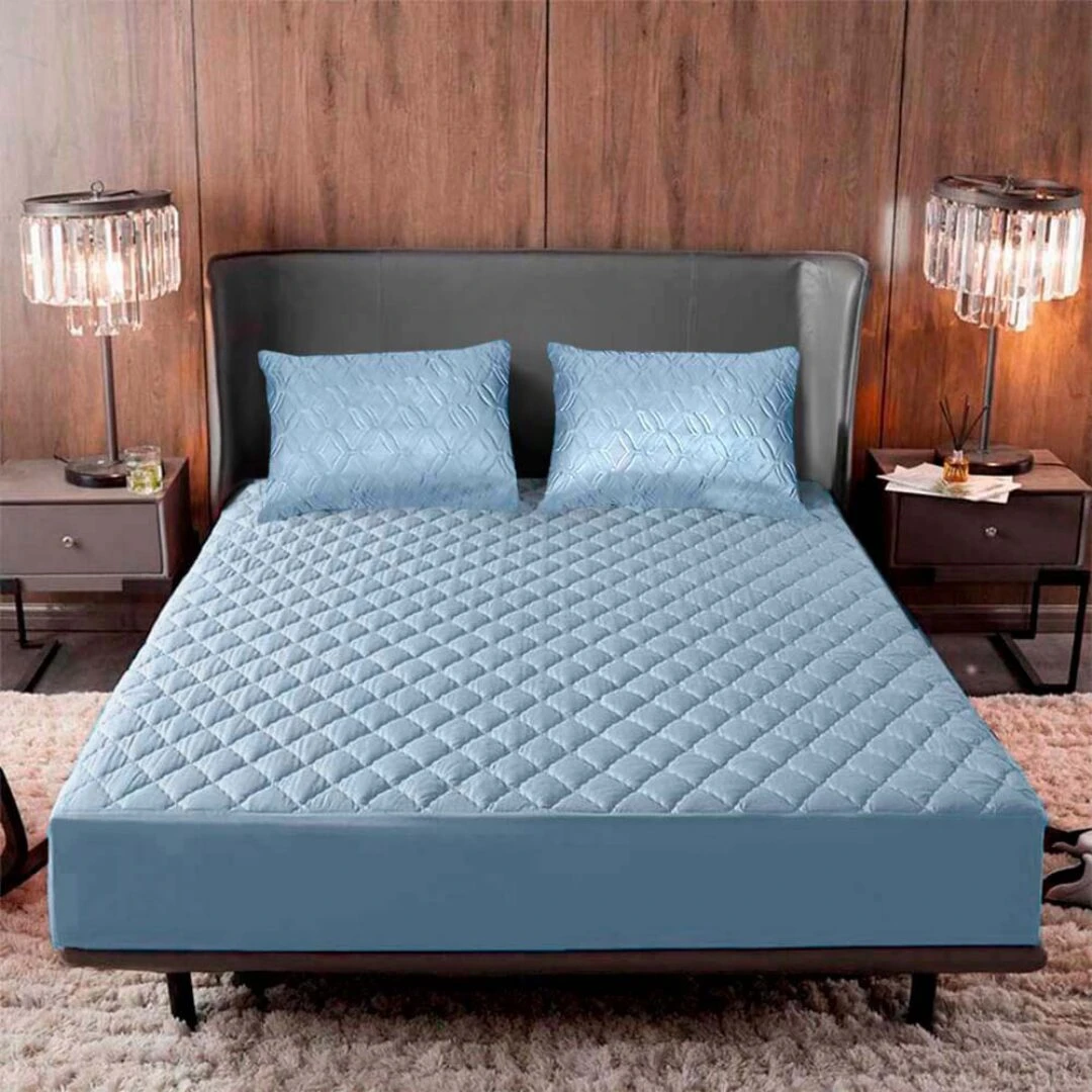 Protector impermeable ultrasuave para colchón 200x200 cm en color azul claro, con textura de rombos y dos almohadas a juego sobre cama con cabecera gris.