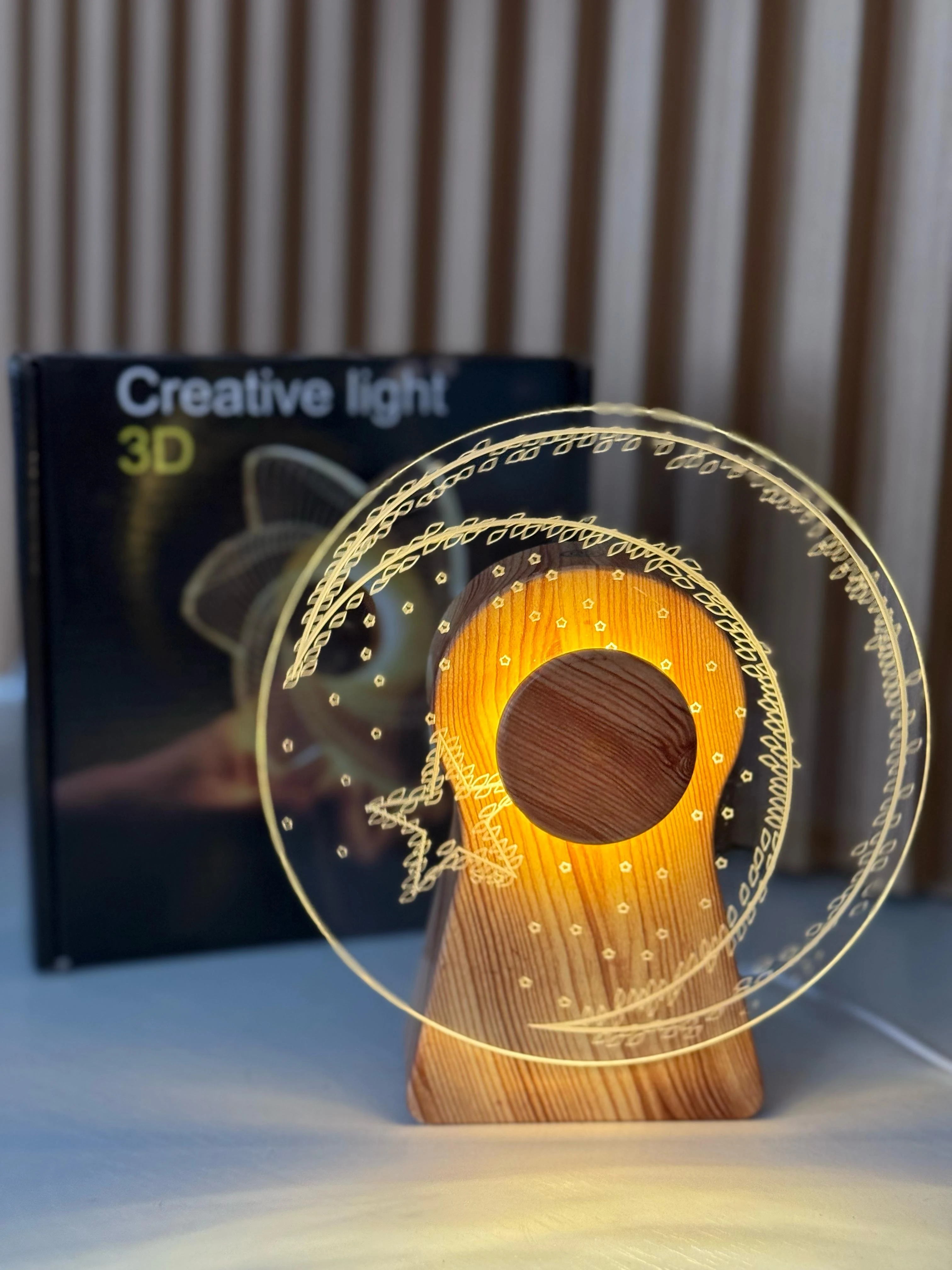 Lámpara 3D giratoria de acrílico con diseño de llave y espiral dorada, montada sobre base de madera, junto a su caja de presentación.