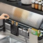 Platillera escurridora de aluminio con tapa protectora, mostrando su instalación bajo estantería, con organizador de cuchillos y accesorios colgantes visibles.