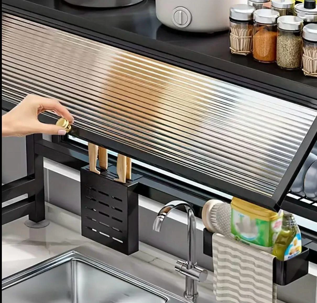 Platillera escurridora de aluminio con tapa protectora, mostrando su instalación bajo estantería, con organizador de cuchillos y accesorios colgantes visibles.
