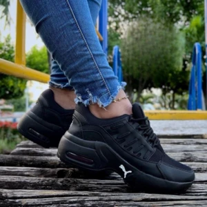 Zapatillas Puma Araña negras con suela acolchada, vista lateral en uso sobre madera, con detalles de malla y logo visible.