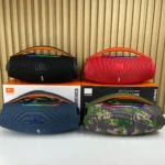 Cuatro altavoces portátiles JBL Boombox 3 en colores negro, rojo, azul y camuflaje, sobre sus cajas originales, con asas ergonómicas y acabado mate.