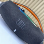 Altavoz portátil JBL Boombox 3 en color gris oscuro con detalles naranjas y luces multicolores en la parte superior.