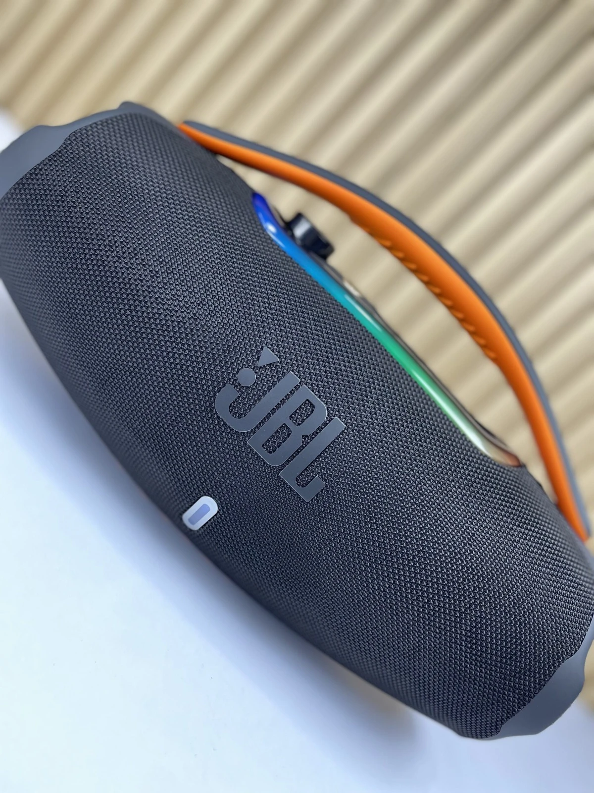Altavoz portátil JBL Boombox 3 en color gris oscuro con detalles naranjas y luces multicolores en la parte superior.