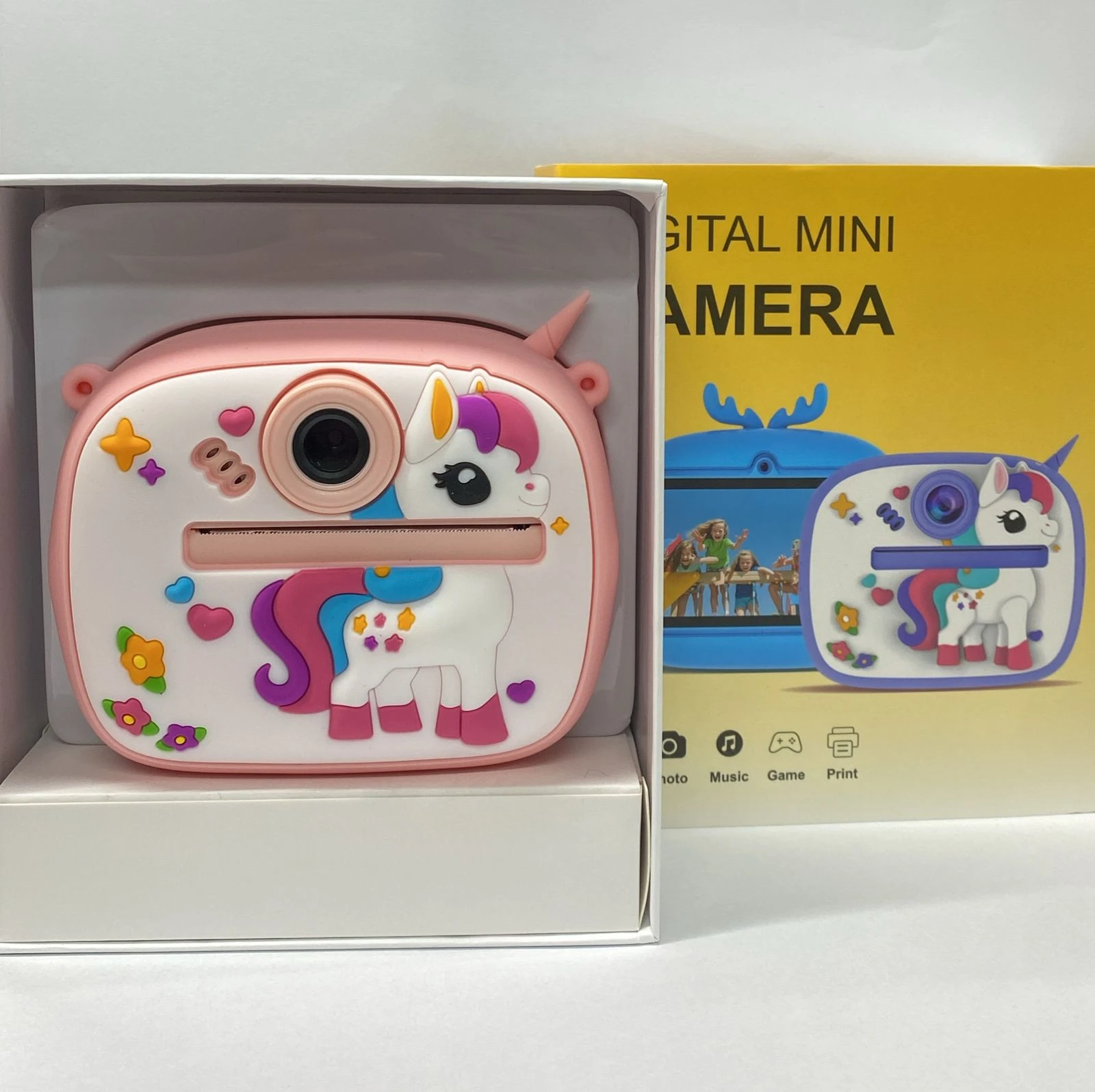 Cámara digital infantil rosa con diseño de unicornio, en su caja abierta mostrando el producto y empaque amarillo con ilustraciones.