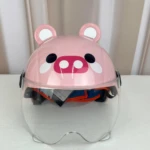 Casco infantil rosa con diseño de cerdito, visor transparente y orejas decorativas, sobre superficie blanca.
