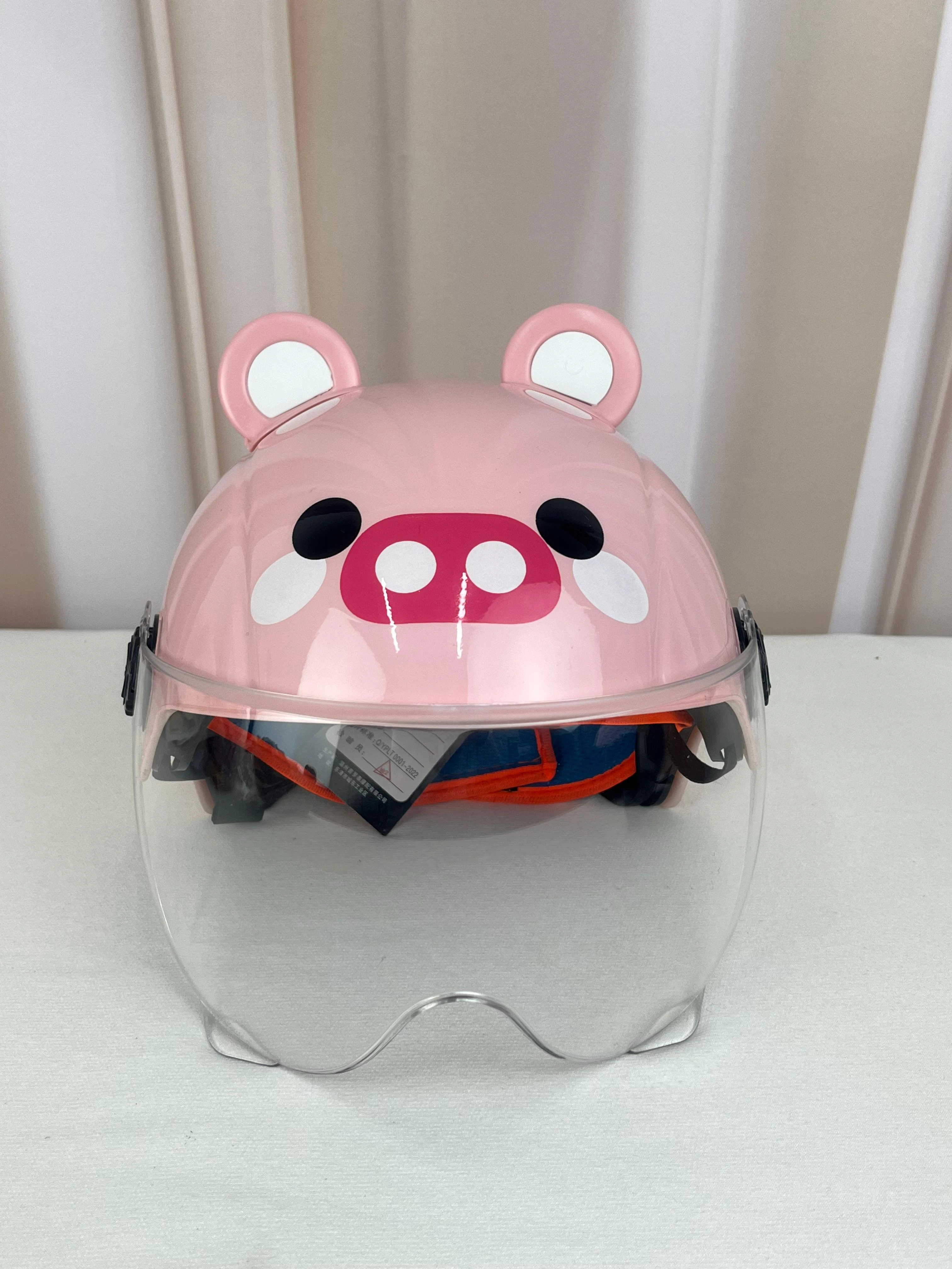 Casco infantil rosa con diseño de cerdito, visor transparente y orejas decorativas, sobre superficie blanca.