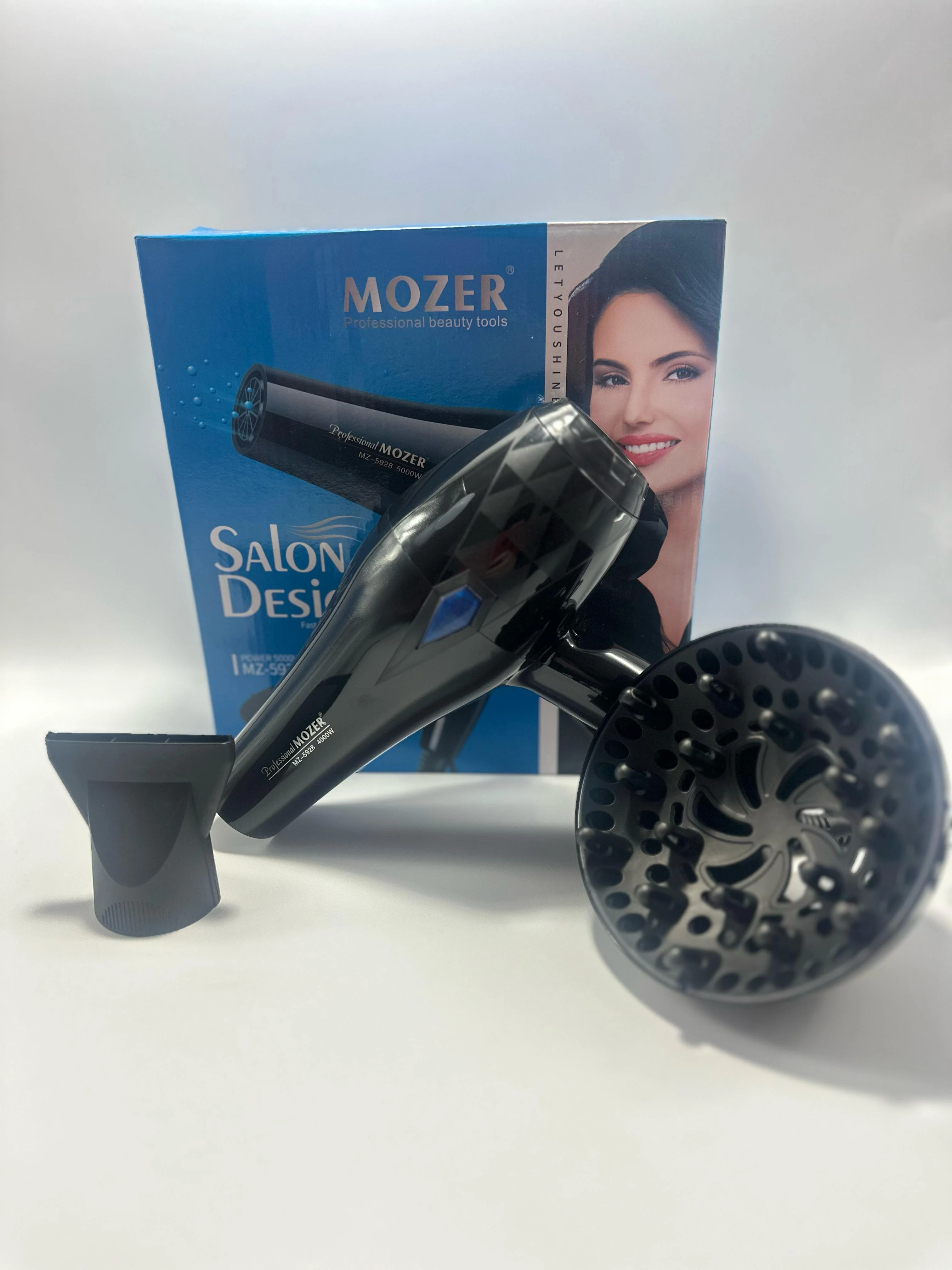 Secadora Mozer MZ5928 compacta en color negro, con difusor y boquilla incluidos, sobre su caja azul con modelo Salon Design.