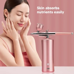 Aerógrafo portátil en rosa metálico con depósito superior y mango ergonómico, sobre fondo rosa pálido.