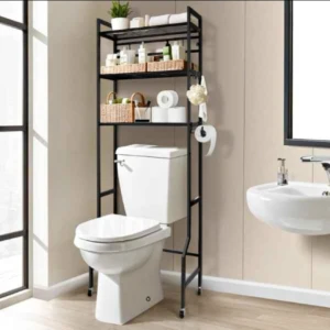 Organizador metálico negro de tres niveles sobre inodoro, con estantes de mimbre y accesorios de baño, en baño moderno con piso de madera y lavabo blanco.