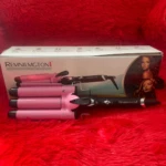 Rizador cerámico de tres tubos color rosa y negro para ondas de sirena, junto a su caja sobre una superficie roja de textura suave.