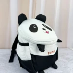 Mochila infantil panda con diseño 3D, color blanco y negro, malla lateral y correas de seguridad visibles.