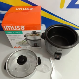 Arrocera Imusa de 1 libra con vaporera, tapa de vidrio y cuchara blanca, mostrada junto a su caja naranja sobre fondo blanco.