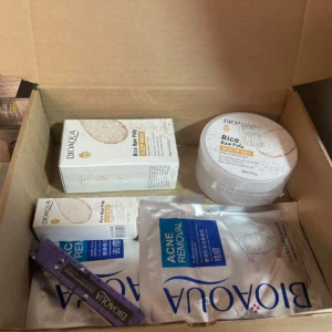 Caja abierta con set de cuidado facial Bioaqua: mascarilla de arroz, suero para pestañas y productos adicionales, dispuestos en interior de caja de cartón marrón.