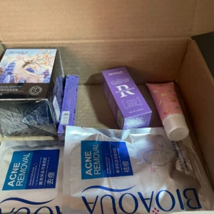 Vista interior de caja abierta mostrando kit de cuidado de la piel Bioaqua Bronce 2, con base, serums y accesorios en tonos púrpura, rosa y azul.