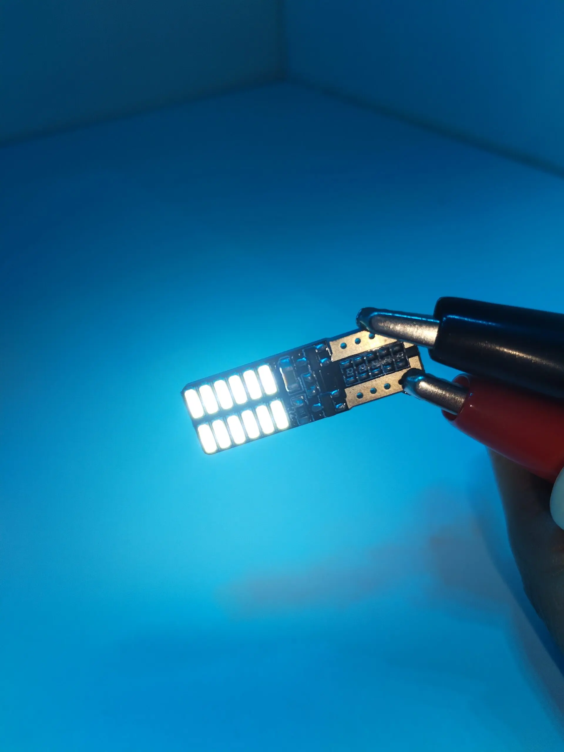 Paleta LED Cocuyo 12V encendida, con diodos blancos y clips de conexión, sobre fondo azul.