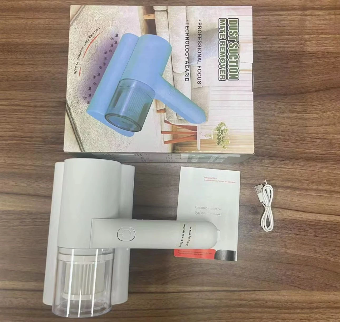 Aspiradora de mano portátil en color blanco, con depósito transparente y cable incluido, junto a su caja y manual. Ideal para limpieza de sábanas y tapicería.
