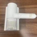 Aspiradora de mano portátil blanca con filtro HEPA visible, sobre superficie de madera. Diseño compacto con mango ergonómico y botón central.