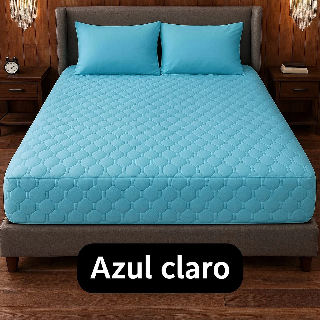 Protector de colchón azul claro con textura hexagonal acolchada, sobre cama con cabecero gris y mesitas de noche en habitación con iluminación cálida.