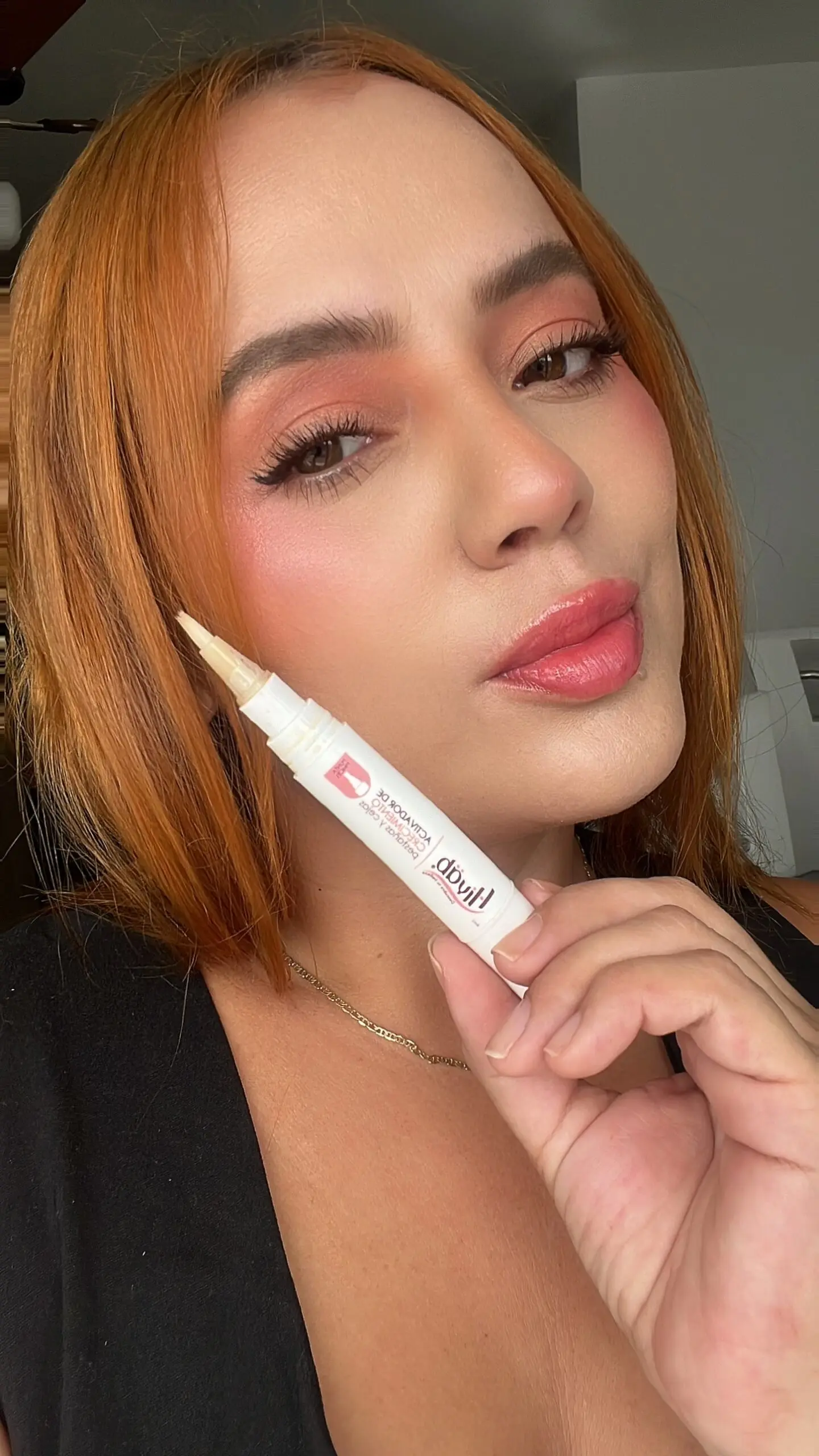 Mujer con maquillaje natural sosteniendo activador de crecimiento pestañas y cejas en presentación tipo lápiz blanco con punta fina.