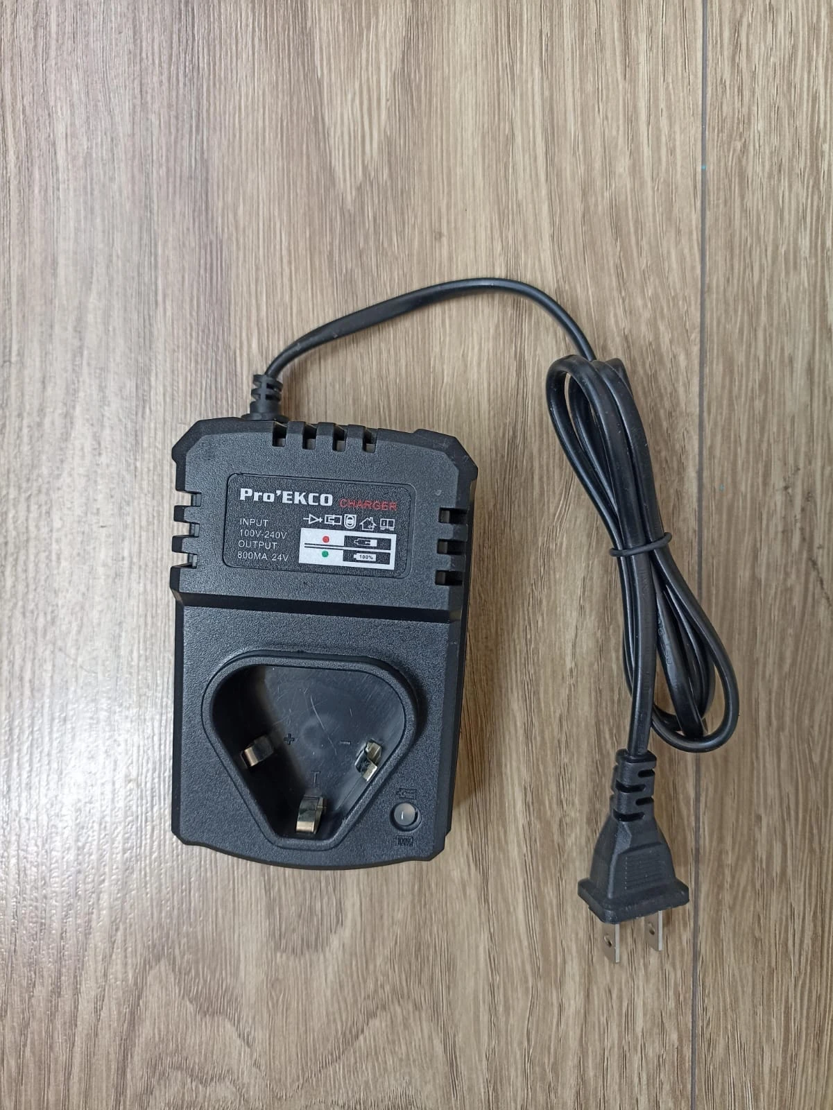 Cargador de batería ProTekco para taladro inalámbrico, color negro, con cable enrollado y enchufe tipo UK, sobre superficie de madera.