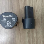 Batería Makita 18V Li-ion de 1.5Ah con etiqueta de reciclaje y número de serie, junto a su base de carga negra sobre superficie de madera.