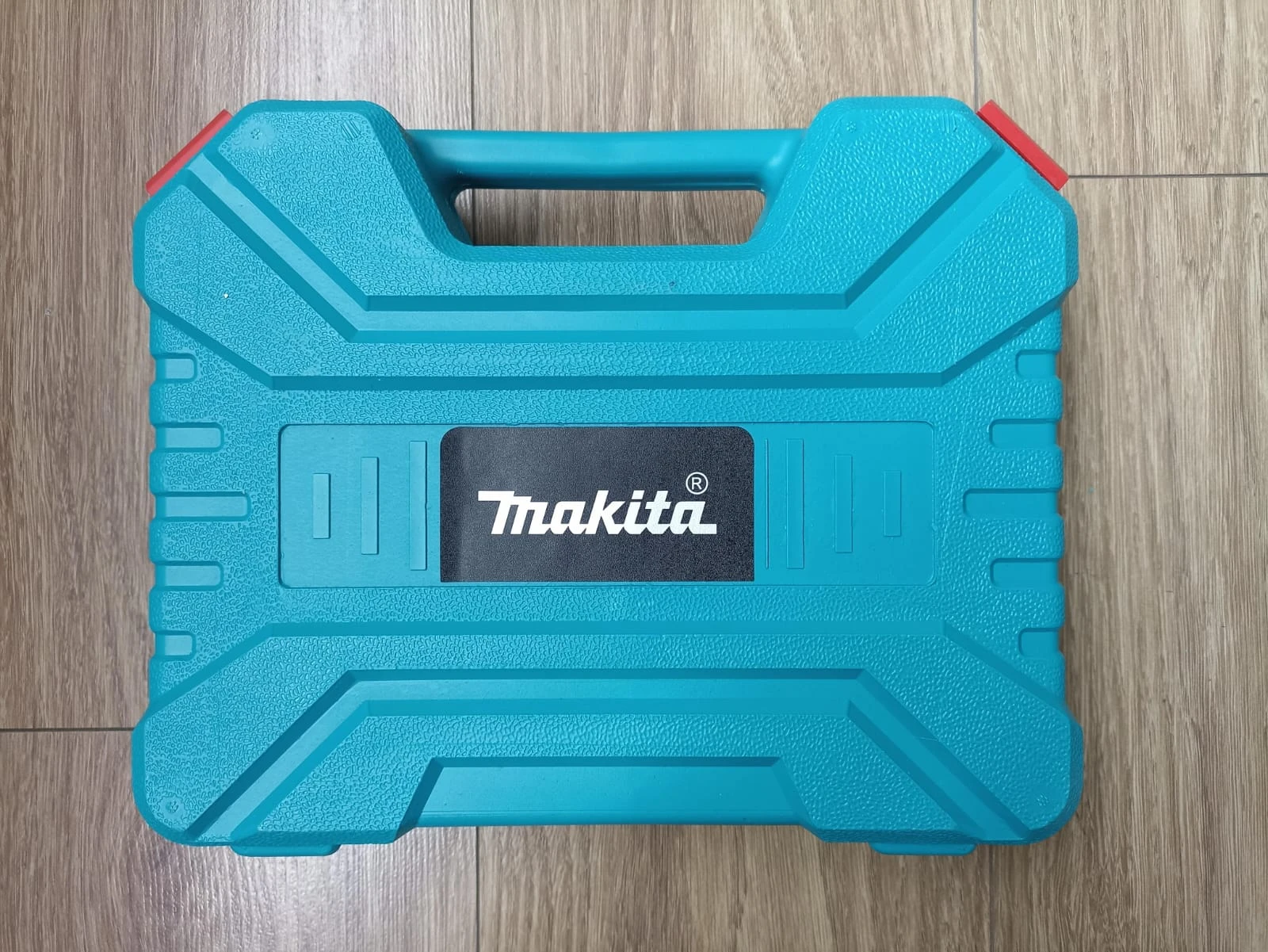 Caja de transporte azul Makita con asas y cierre rojo, sobre superficie de madera.