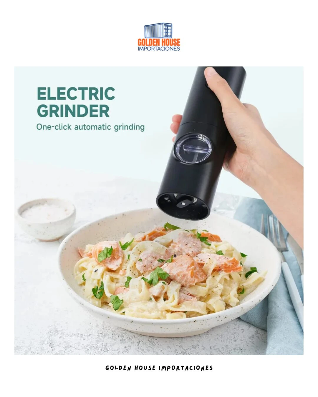 Molino eléctrico negro con tapa transparente, en uso sobre plato de pasta con salmón y hierbas, en mano derecha, sobre mesa clara con salero al fondo.