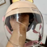 Casco juvenil color beige con orejas de capibara y visor transparente extendido, mostrando detalles internos y sistema de sujeción rosa.